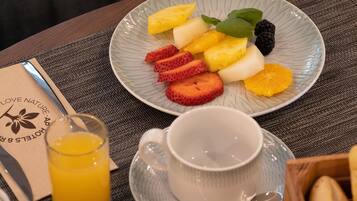 Une assiette de fruits comprenant des fraises, de l’ananas et des mûres, un verre de jus d’orange et une tasse posée sur une table.