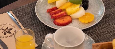 A plate of fruit including strawberries, pineapple, and blackberries, a glass of orange juice, and a cup on a table.
