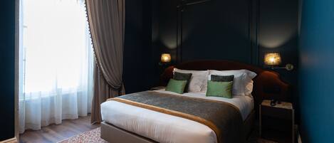 Une chambre à coucher avec un grand lit, une table de chevet, une lampe et une fenêtre avec des rideaux.
