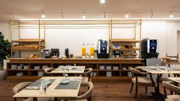 A modern cafe with wooden tables and chairs, a coffee machine, and shelves with dishes and utensils.