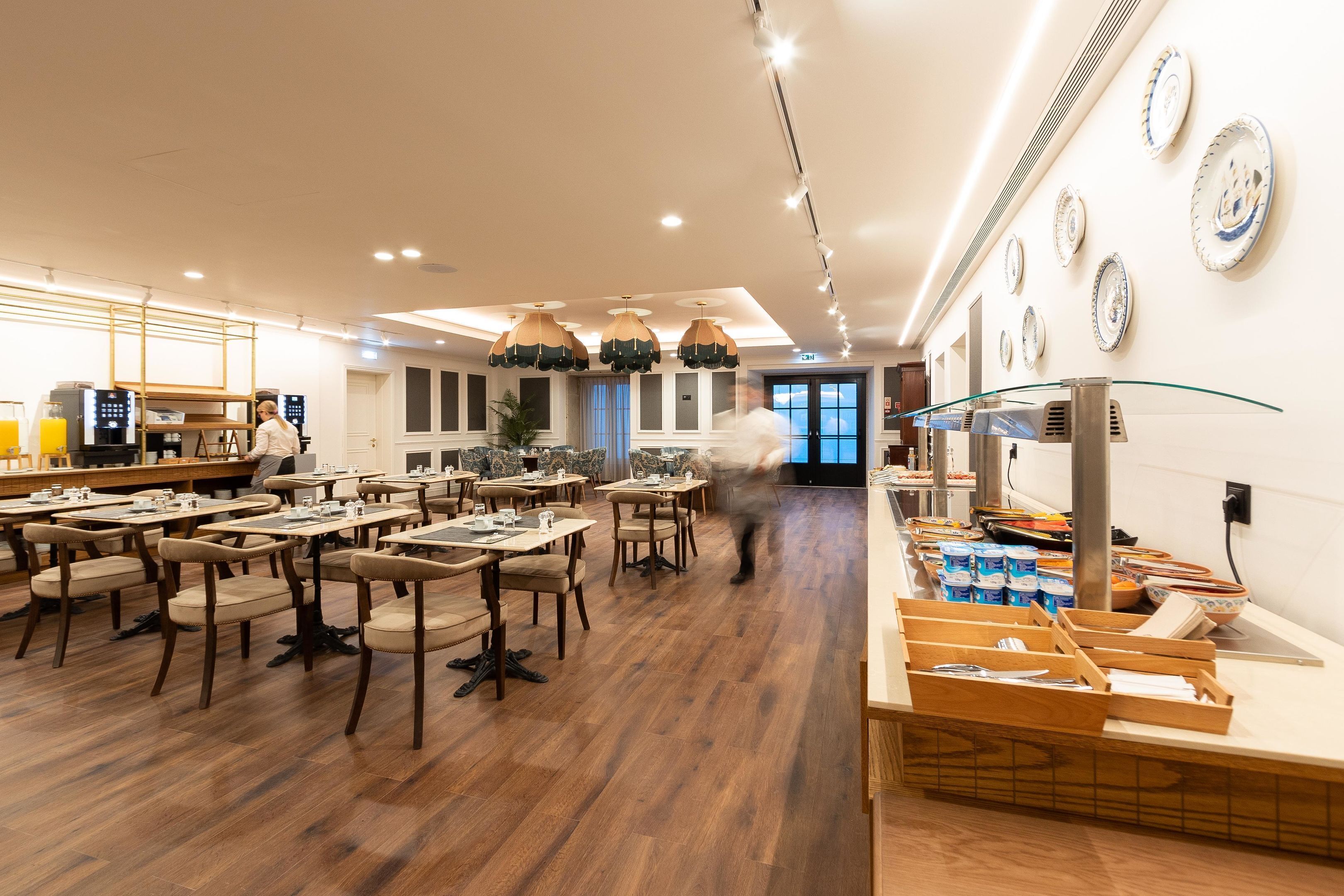 A spacious dining area with wooden tables and chairs, a buffet counter with various food items, and a wall decorated with plates.