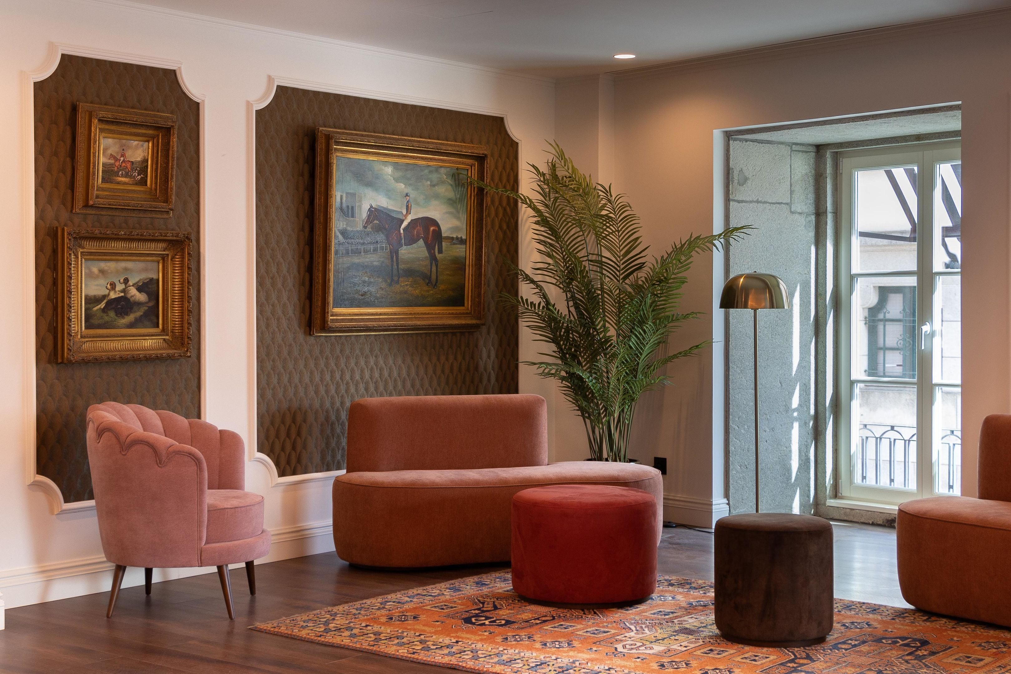 Uma sala de estar moderna com uma grande janela, um banquinho vermelho, uma poltrona rosa e uma pintura grande na parede.
