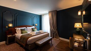 A modern hotel room with a large bed, bedside lamps, a small table with cups and a kettle, and a view of the outdoors through a window.