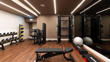 Un gimnasio con equipamiento de levantamiento de pesas, bancos y pelotas de ejercicio.