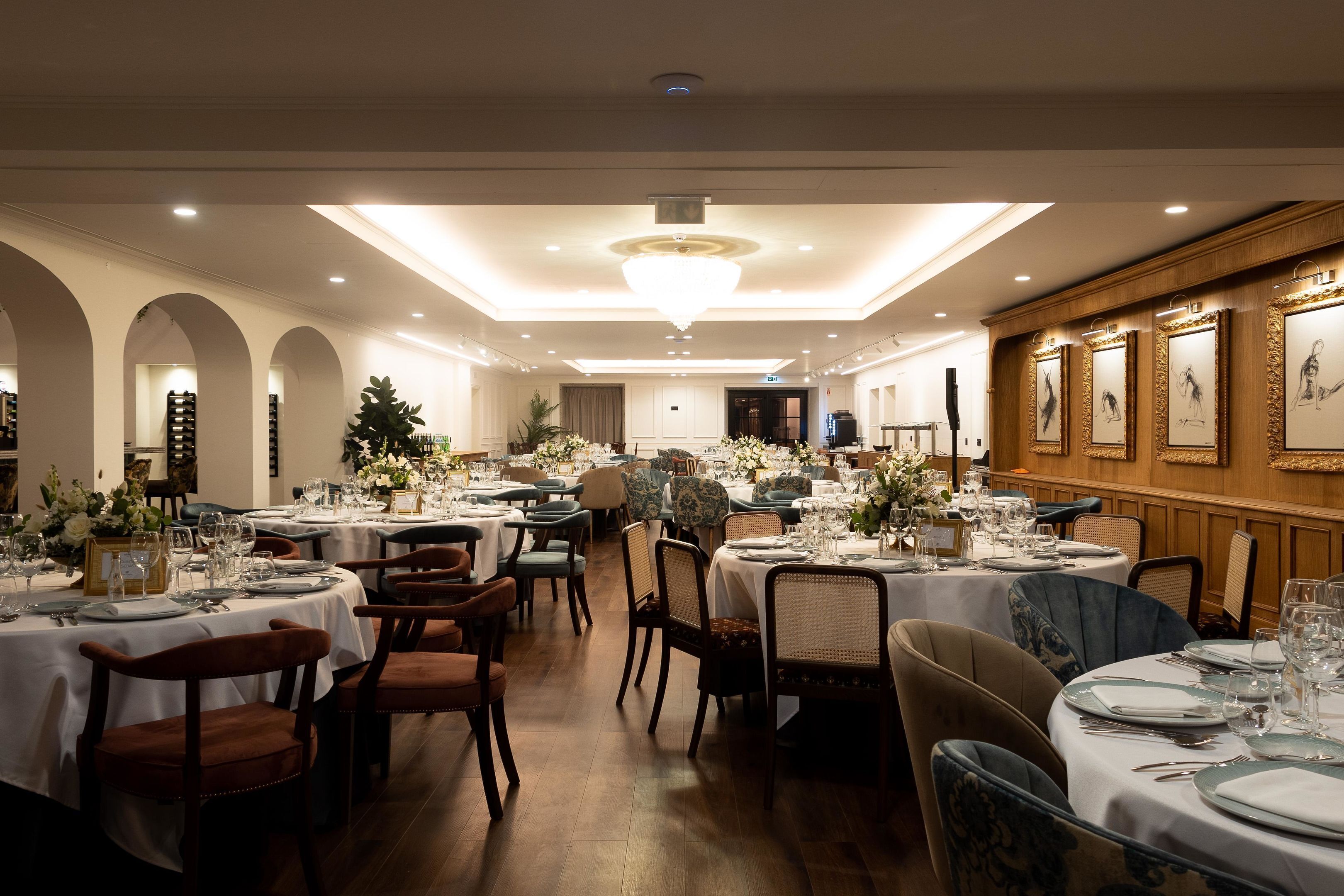 A banquet hall with round tables set for dining, featuring white tablecloths and floral centerpieces.
