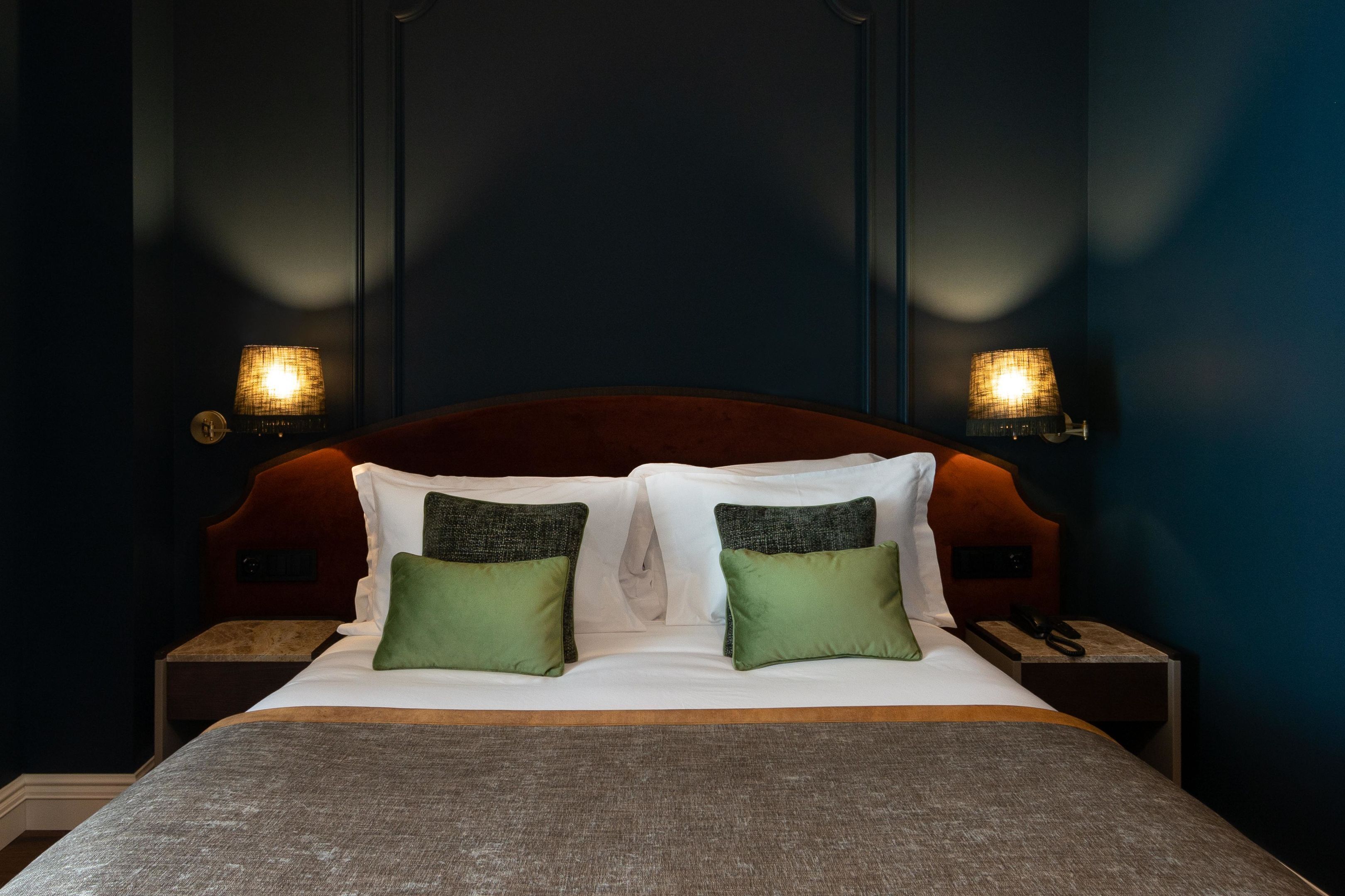 A neatly made bed with white and green pillows, a dark headboard, and two bedside lamps.