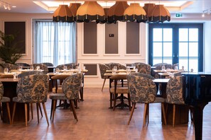 A dining area with multiple tables and chairs, a piano, and large windows with curtains. - AP Dona Aninhas  (Viana do Castelo)