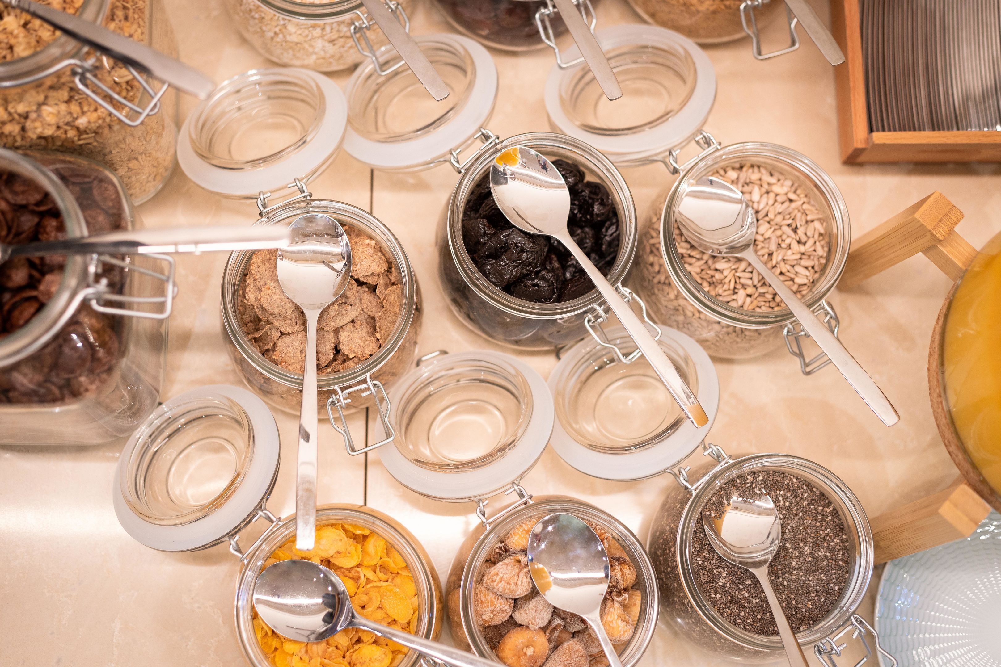 A variety of food items in glass containers with metal lids and spoons, arranged on a table.