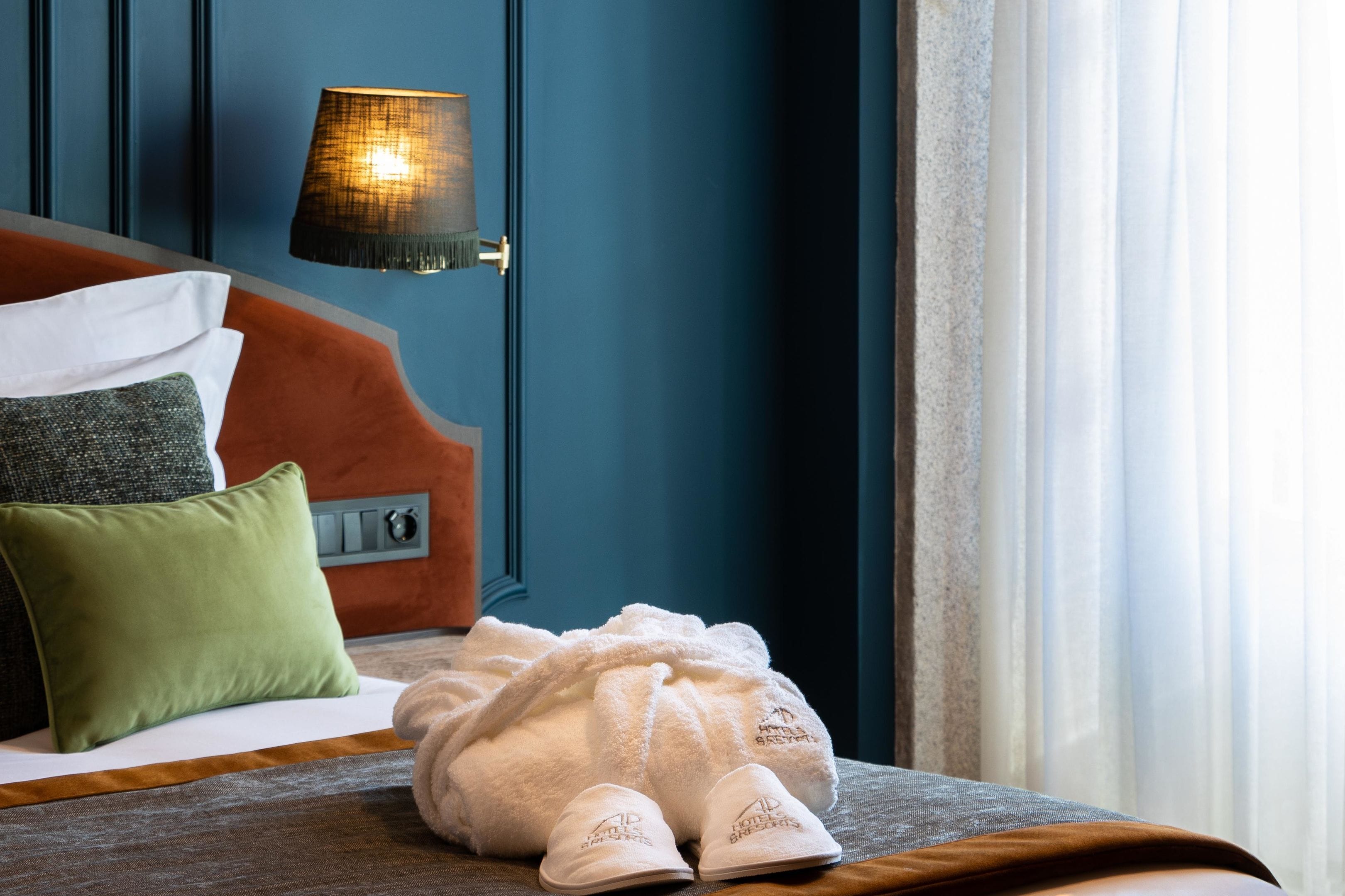 Una cama bien hecha con un albornoz blanco y zapatillas, una almohada verde y un cabecero rojo.