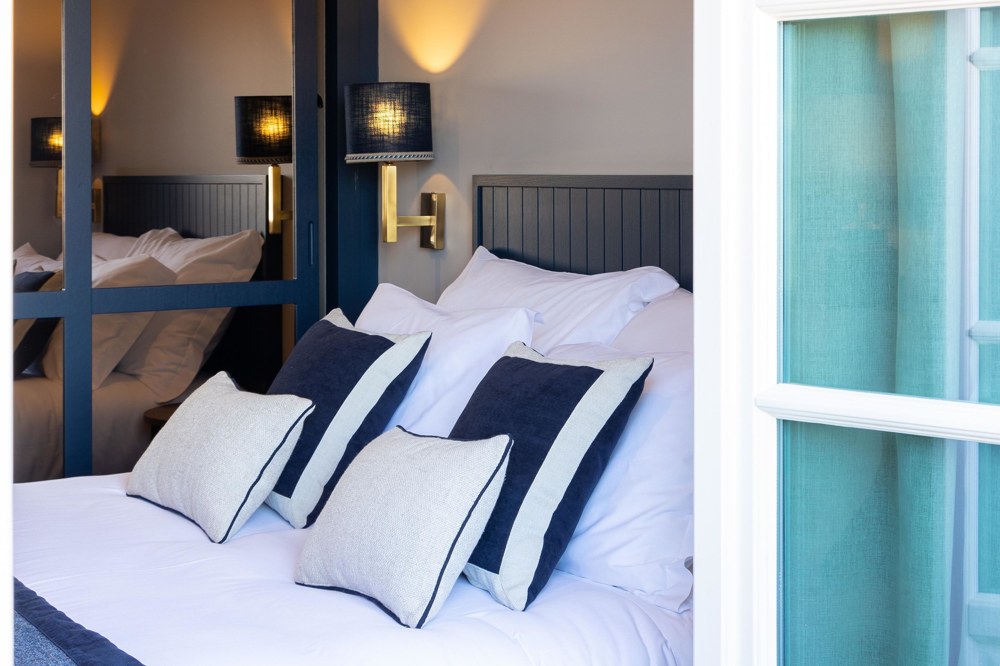 A neatly made bed with white and navy pillows, a wooden headboard, and a wall-mounted lamp.