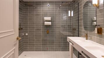 Une salle de bain moderne dotée d’une douche à l’italienne, d’un grand miroir et d’un meuble-lavabo blanc avec un robinet doré.