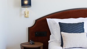 A neatly made bed with a brown headboard, a bedside table with a phone, and a wall-mounted lamp. - AP Dona Aninhas  (Viana do Castelo)