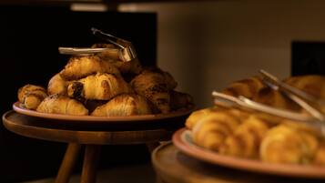 Una mesa de buffet con platos de pasteles, incluyendo cruasanes y otras preparaciones horneadas, con unas pinzas al lado.