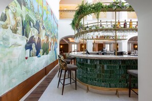 Uma área de bar com balcão em mosaico, banquetas e um mural na parede.