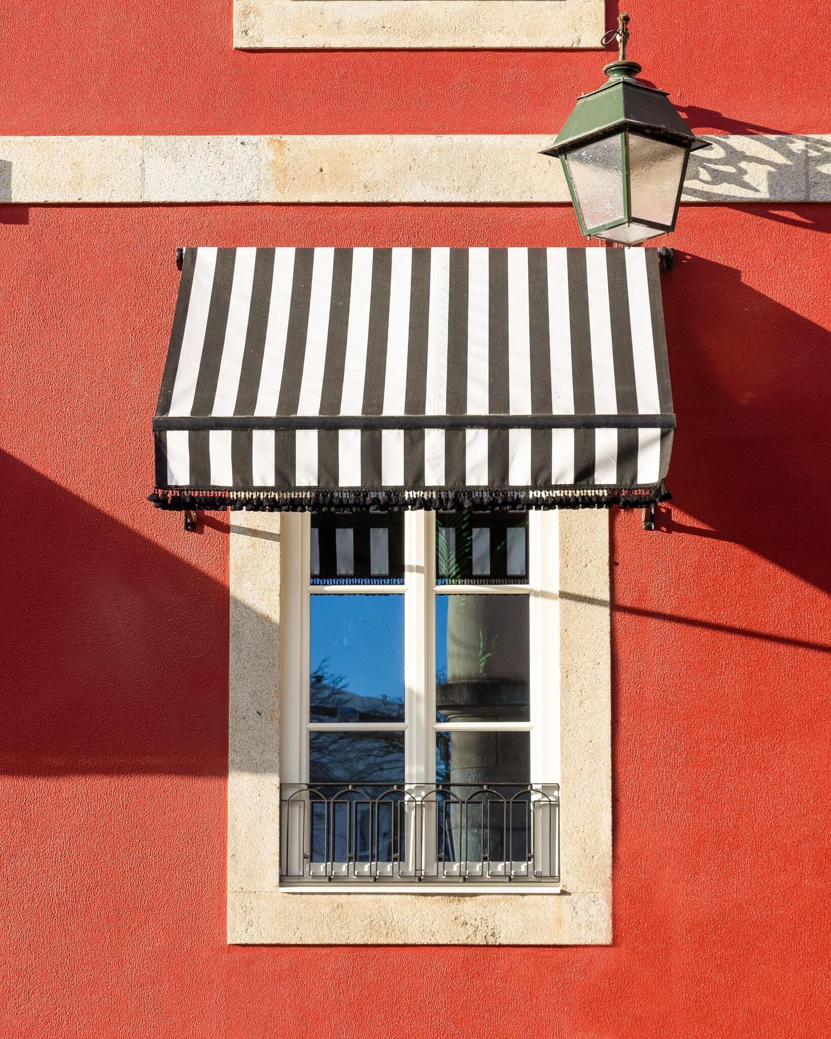 A window with a black and white striped awning and a green street lamp above it.