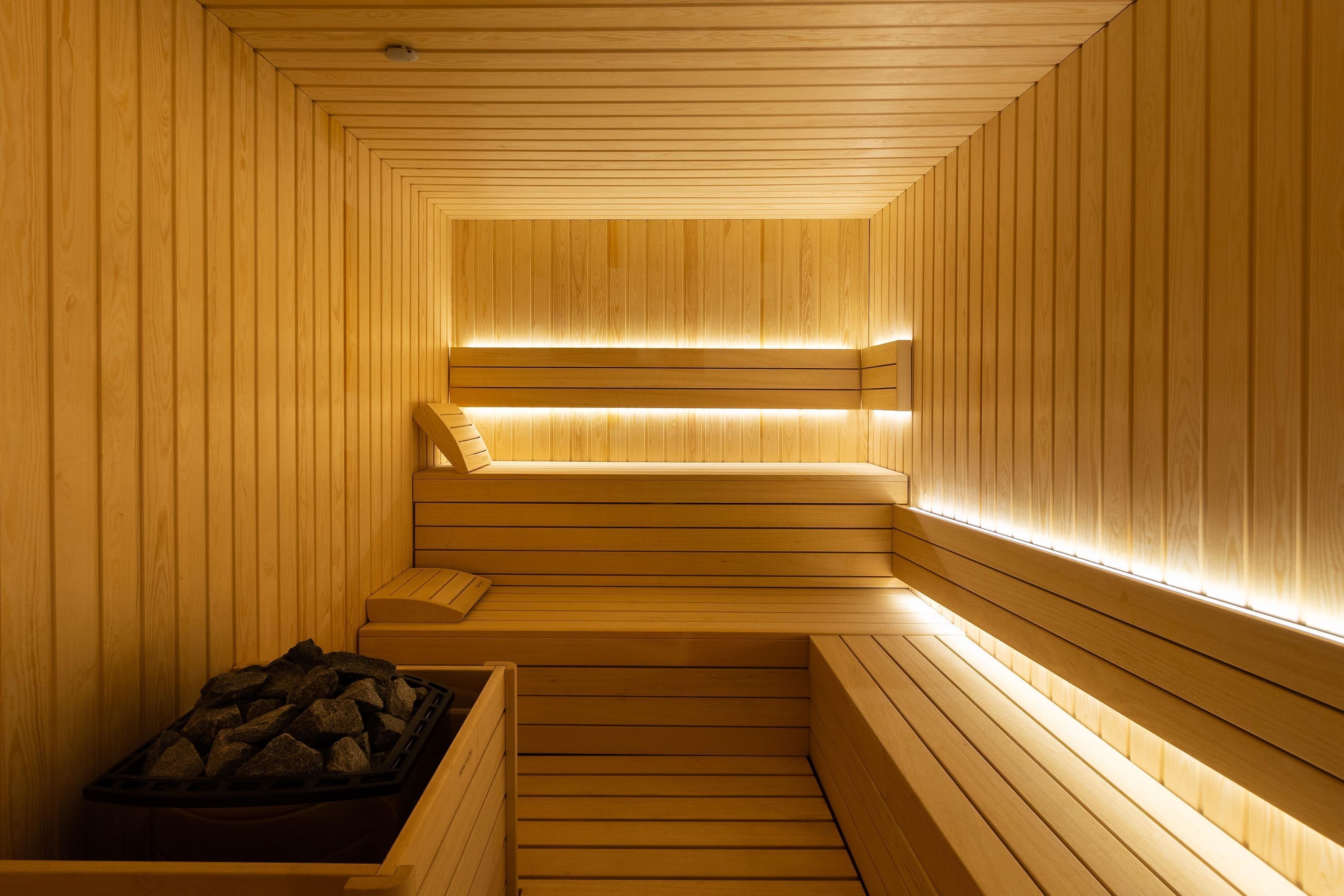 A wooden sauna with benches and a bench for sitting, and a container with rocks.