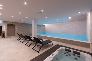 A modern indoor pool area with black lounge chairs, a hot tub, and a blue pool. - AP Dona Aninhas  (Viana do Castelo)