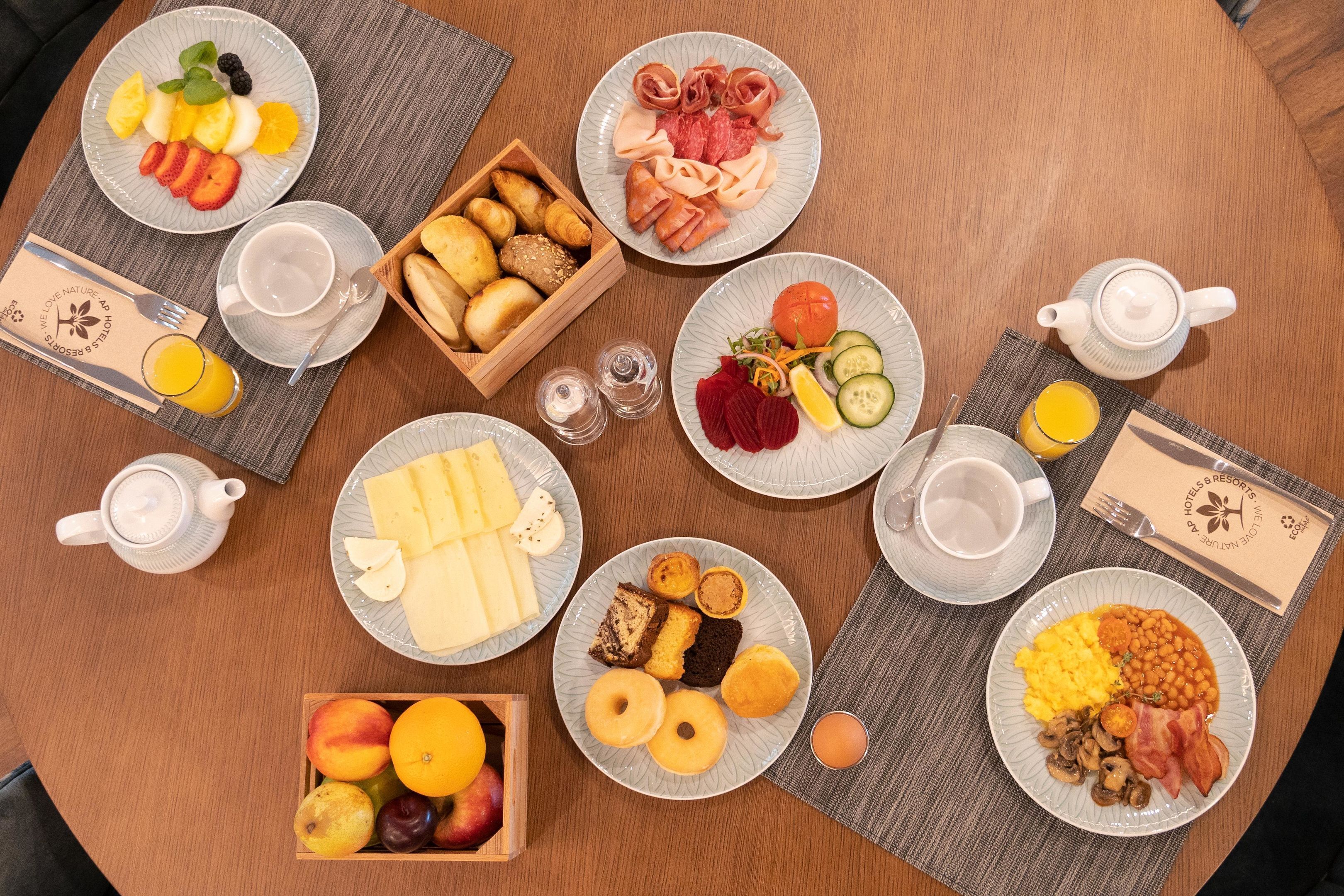 Uma mesa de café da manhã com vários pratos de comida, um bule de chá e uma cesta de frutas.