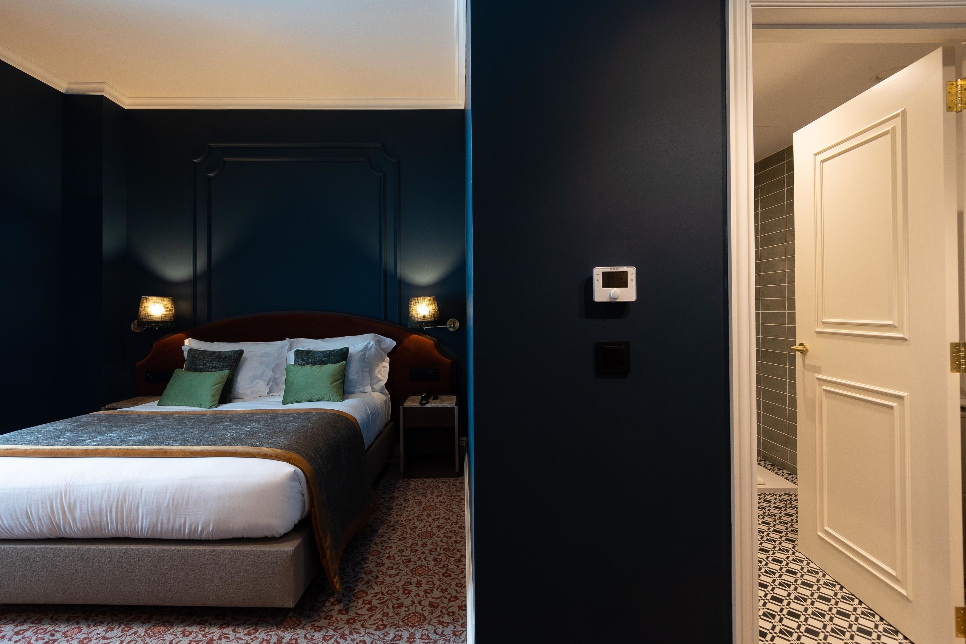 Un dormitorio con cama, mesitas de noche e iluminación en la pared.