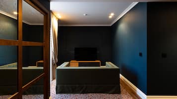 A modern room with a dark blue wall, a wooden floor, a green sofa, and a flat-screen TV mounted on the wall.