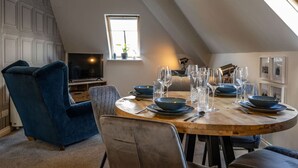 A dining area with a round wooden table set for six, surrounded by blue upholstered chairs. - Old Distillery Apartment in Fort William (Fort William)