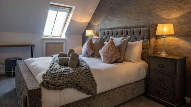 A bedroom with a large bed, a nightstand with a lamp, a window, and a small table. - Old Distillery Apartment in Fort William (Fort William)