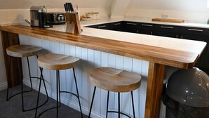 A kitchen with a wooden bar counter, three stools, a coffee maker, and a toaster. - Old Distillery Apartment in Fort William (Fort William)