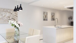 Et moderne køkken med en central ø, et glasbord og hvide skabe.