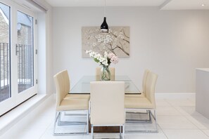 Una sala da pranzo moderna con un tavolo in vetro, sedie beige e un vaso di fiori.