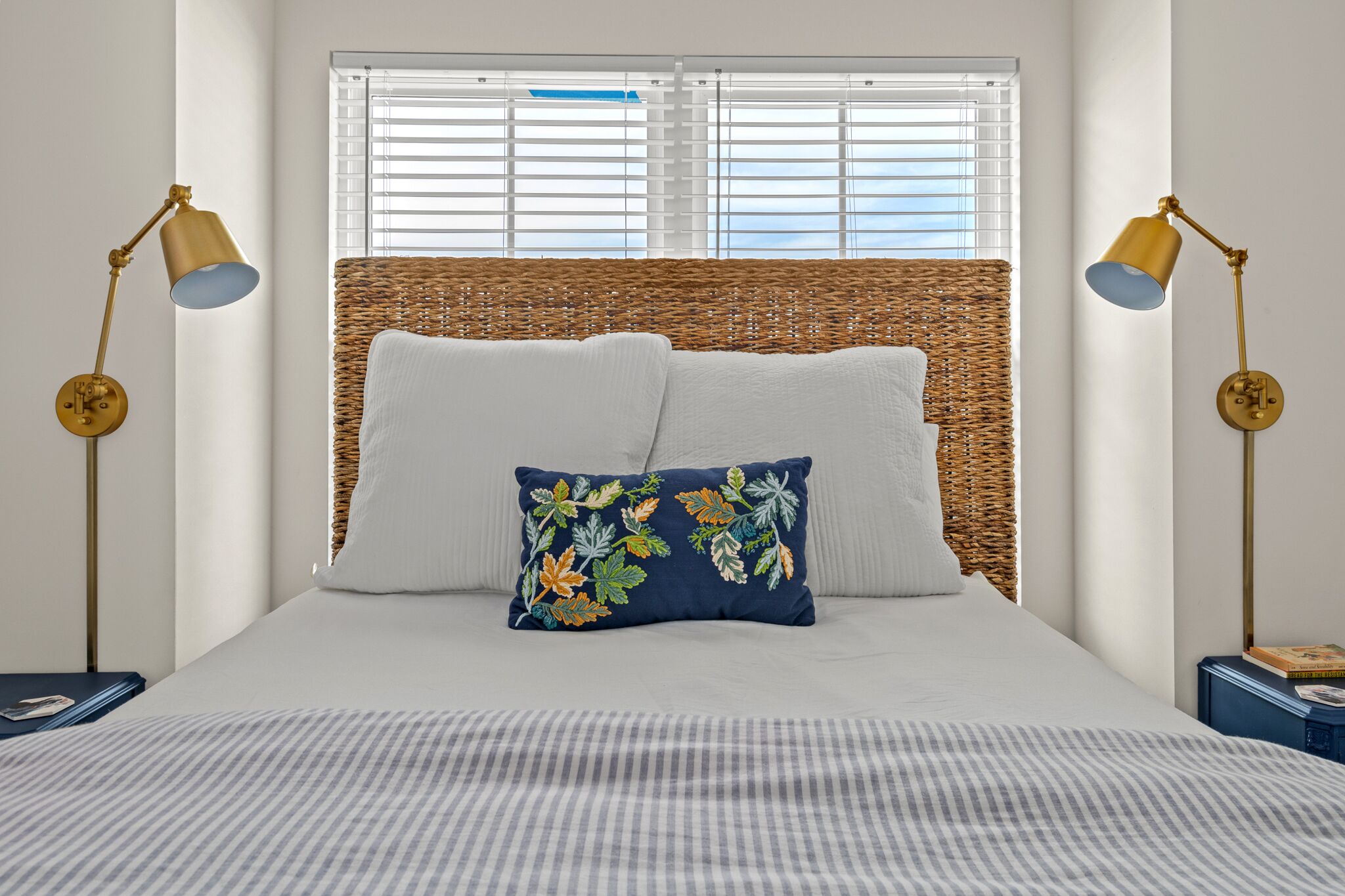 Una cama bien hecha con una colcha a rayas, un cojín decorativo y dos lámparas de noche.