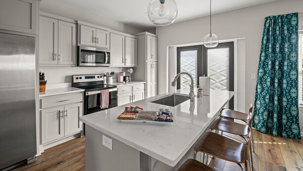 Una cocina moderna con armarios blancos, un refrigerador de acero inoxidable, un microondas y una isla grande con un lavamanos y asientos.