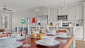 Una cocina moderna con armarios blancos, un refrigerador de acero inoxidable y una zona de comedor con platos y copas de vino blancos.