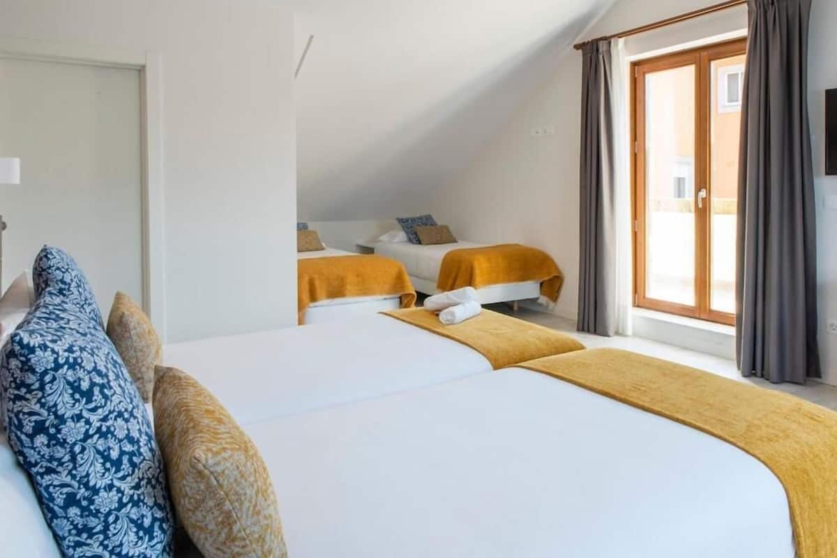 A hotel room with two beds, a large window with curtains, and a view of the outside.