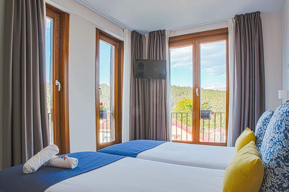 A hotel room with two beds, a TV, and a balcony with a view.