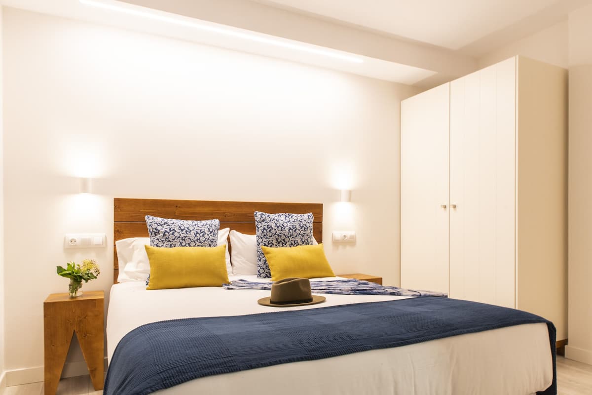 A neatly arranged bedroom with a wooden headboard, two bedside lamps, a bed with a blue blanket, and a wardrobe.