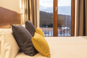 A hotel room with a bed, two pillows, a window with a view of a balcony and trees. - LiresCa (Cee)