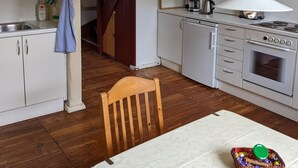 Una cuina amb armaris blancs, una escala de fusta, una taula de dinar amb una cistella i una làmpada penjant.