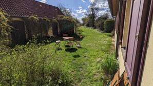 Un pati amb taula i cadires, un edifici amb teulada de rajola, i una zona de jardí.