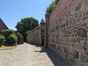 Une rue pavée bordée de murs de pierre, un bâtiment en briques et un arbre.