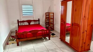 A bedroom with a wooden bed, a wardrobe, and a window with blinds. - Seaside apartment 4 pers Bananier Capesterre B-E (Trois-Rivières)