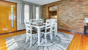 Un comedor con pared de ladrillo, piso de madera y juego de mesa blanco.