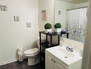 Bathroom features a toilet, sink, and shower, with a shelf for personal items and artwork on the walls.