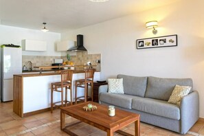 A modern kitchen with a central island, wooden chairs, a grey sofa, and a tiled floor.