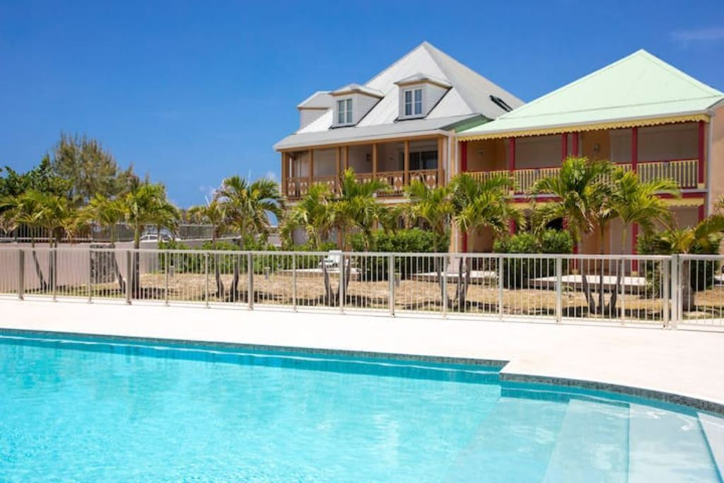 A hotel with a swimming pool, a two-story building, and a fenced area with palm trees.