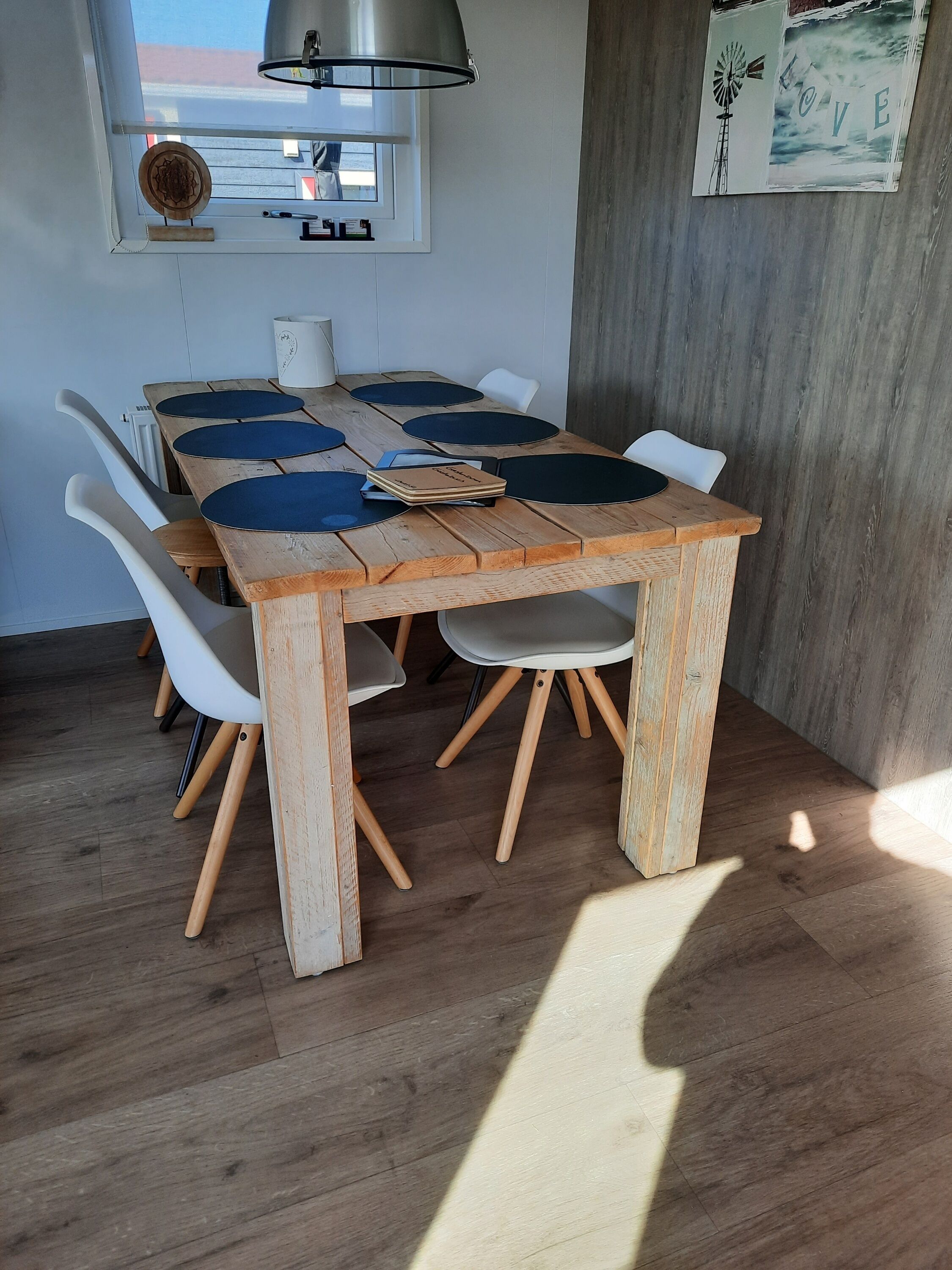 Ein Essbereich mit Holztisch und weißen Stühlen, einer Deckenleuchte und einem Wandbild.