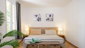 Un dormitorio con cama, dos lámparas de noche, una ventana con cortinas y dos obras de arte colgadas en la pared.