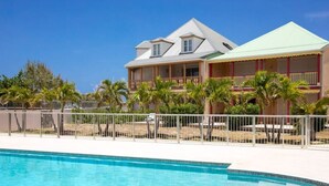 Un hotel con piscina, un edificio de dos pisos y un área cercada con palmeras.