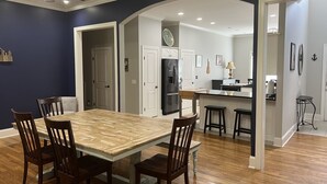 Un comedor con una mesa y sillas de madera, una cocina con refrigerador y estufa, y un arco abierto que da a otra habitación.