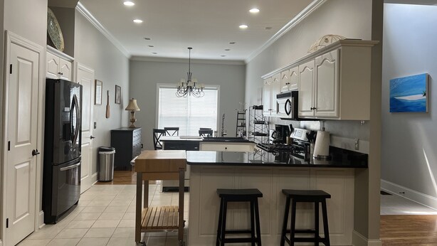 Una cocina moderna con armarios blancos, una isla central con taburetes y un comedor con candelabro.