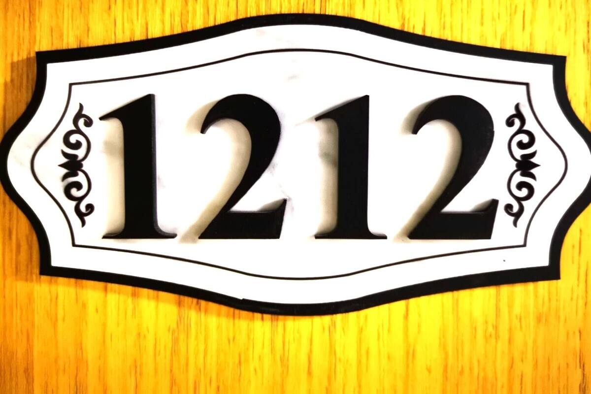 A black and white house number sign with the number 1212 on a wooden background.